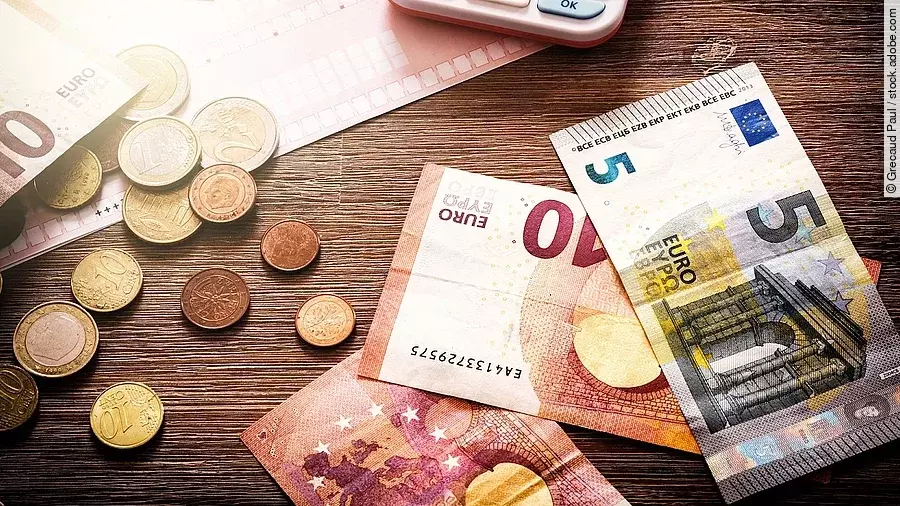 Banknoten Mehrere Geldmünzen, Banknoten und ein Taschenrechner liegen verteilt auf dem Tisch.