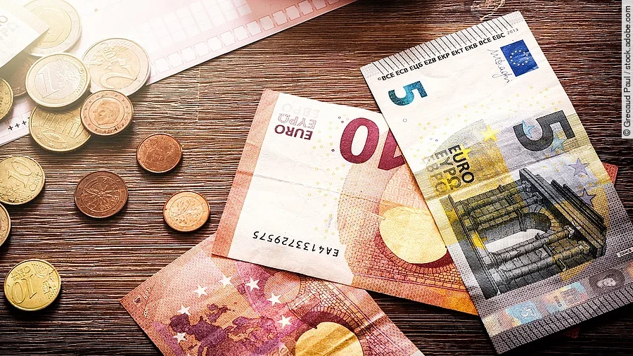 Mehrere Geldmünzen, Banknoten und ein Taschenrechner liegen verteilt auf dem Tisch.