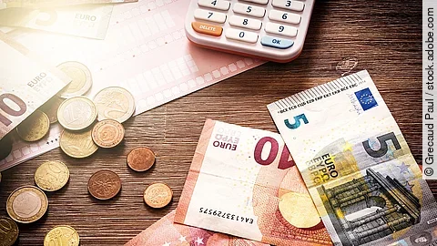 Banknoten Mehrere Geldmünzen, Banknoten und ein Taschenrechner liegen verteilt auf dem Tisch.