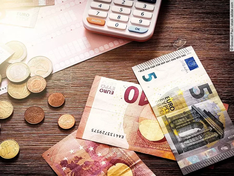 Mehrere Geldmünzen, Banknoten und ein Taschenrechner liegen verteilt auf dem Tisch.