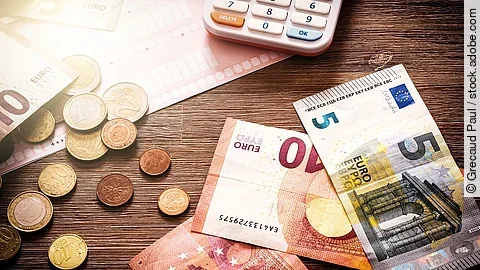 Banknoten Mehrere Geldmünzen, Banknoten und ein Taschenrechner liegen verteilt auf dem Tisch.