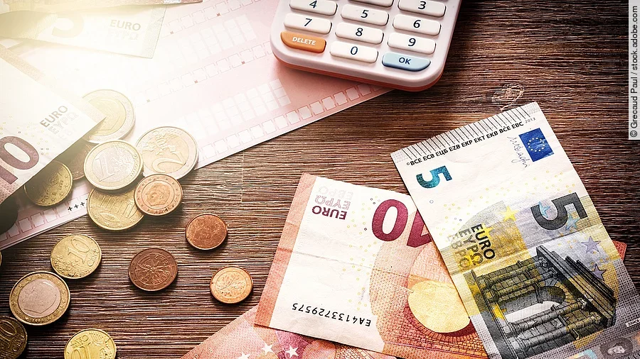 Banknoten Mehrere Geldmünzen, Banknoten und ein Taschenrechner liegen verteilt auf dem Tisch.