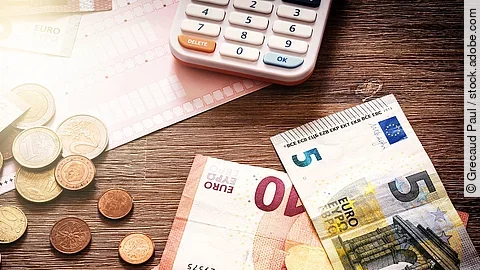 Banknoten Mehrere Geldmünzen, Banknoten und ein Taschenrechner liegen verteilt auf dem Tisch.