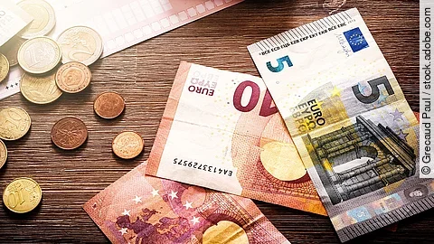 Banknoten Mehrere Geldmünzen, Banknoten und ein Taschenrechner liegen verteilt auf dem Tisch.