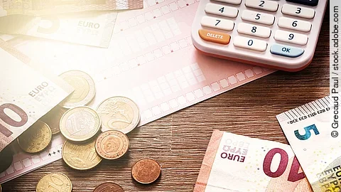 Banknoten Mehrere Geldmünzen, Banknoten und ein Taschenrechner liegen verteilt auf dem Tisch.