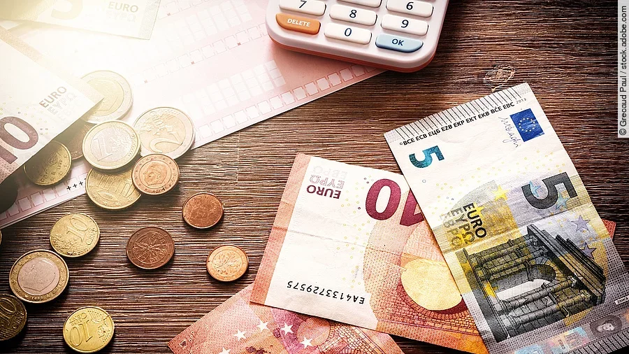 Banknoten Mehrere Geldmünzen, Banknoten und ein Taschenrechner liegen verteilt auf dem Tisch.