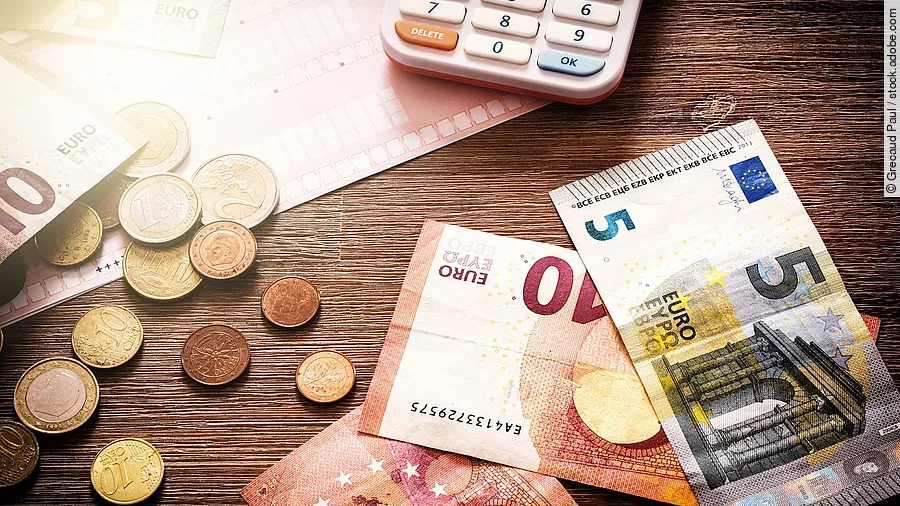 Banknoten Mehrere Geldmünzen, Banknoten und ein Taschenrechner liegen verteilt auf dem Tisch.