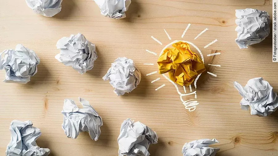 Viele zusammengeknüllte Blätter Papier. Eines davon in gelber Farbe und umrahmt wie eine leuchtende Glühbirne.