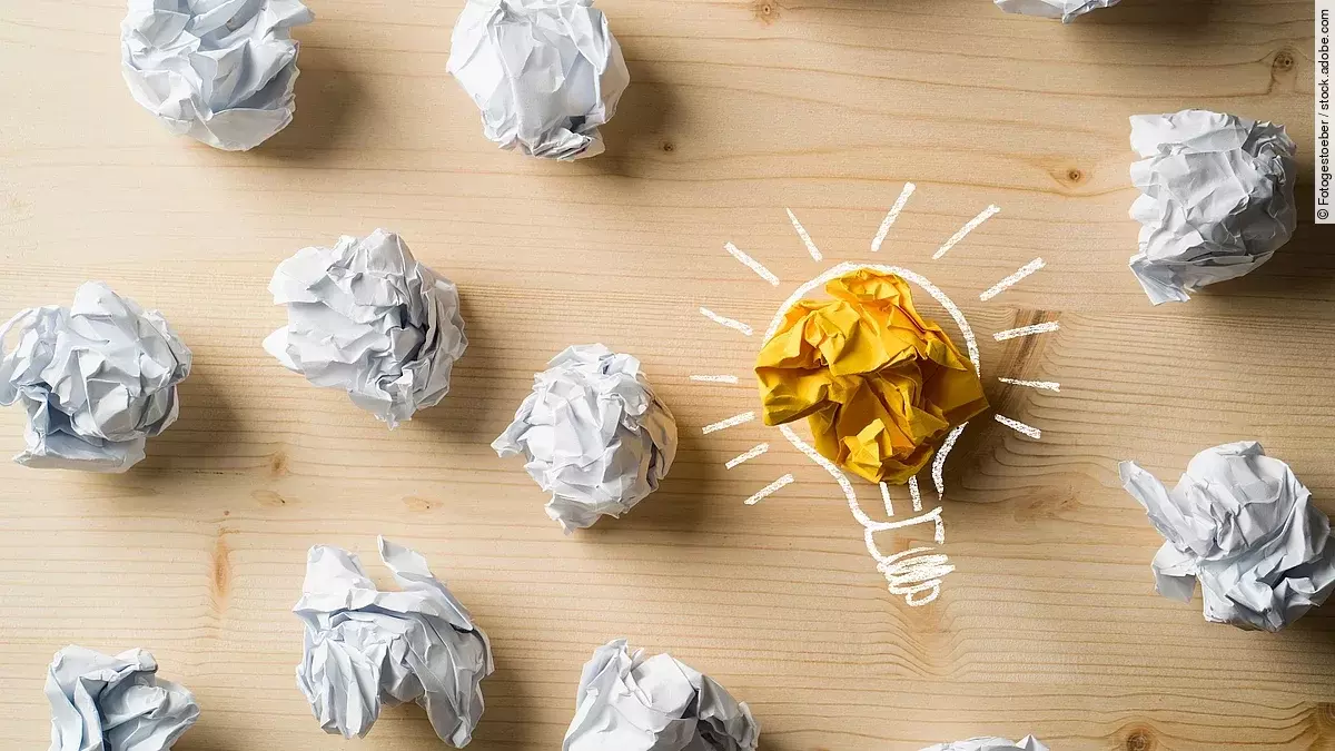 Ideen Viele zusammengeknüllte Blätter Papier. Eines davon in gelber Farbe und umrahmt wie eine leuchtende Glühbirne.