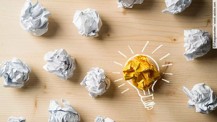 Ideen Viele zusammengeknüllte Blätter Papier. Eines davon in gelber Farbe und umrahmt wie eine leuchtende Glühbirne.