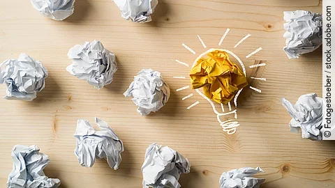 Viele zusammengeknüllte Blätter Papier. Eines davon in gelber Farbe und umrahmt wie eine leuchtende Glühbirne.