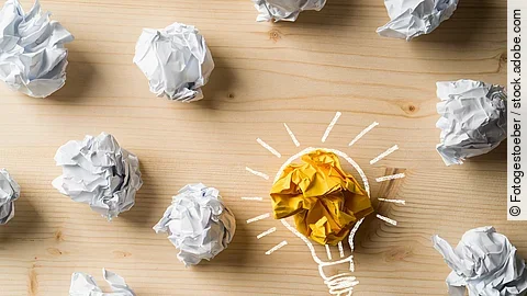 Ideen Viele zusammengeknüllte Blätter Papier. Eines davon in gelber Farbe und umrahmt wie eine leuchtende Glühbirne.