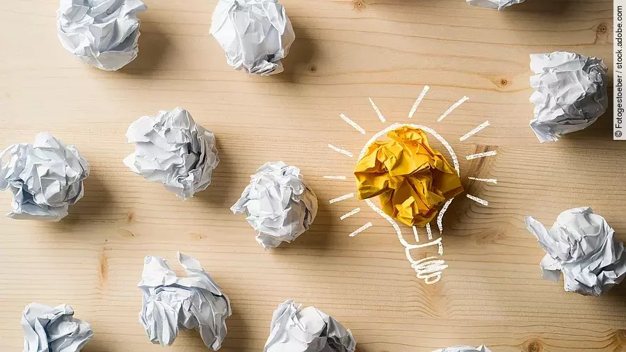 Ideen Viele zusammengeknüllte Blätter Papier. Eines davon in gelber Farbe und umrahmt wie eine leuchtende Glühbirne.