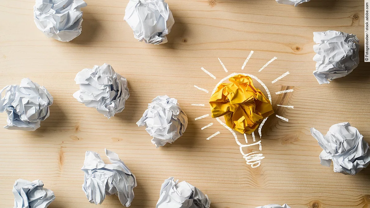 Ideen Viele zusammengeknüllte Blätter Papier. Eines davon in gelber Farbe und umrahmt wie eine leuchtende Glühbirne.