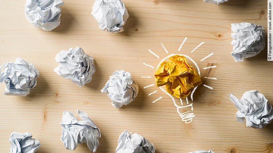 Ideen Viele zusammengeknüllte Blätter Papier. Eines davon in gelber Farbe und umrahmt wie eine leuchtende Glühbirne.