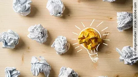 Viele zusammengeknüllte Blätter Papier. Eines davon in gelber Farbe und umrahmt wie eine leuchtende Glühbirne.