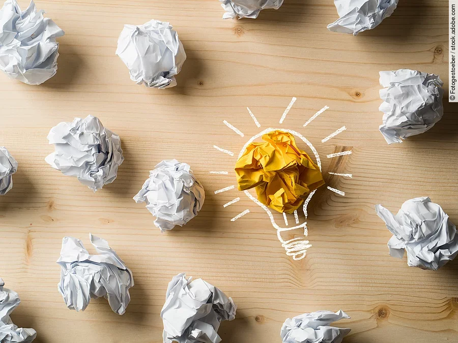 Viele zusammengeknüllte Blätter Papier. Eines davon in gelber Farbe und umrahmt wie eine leuchtende Glühbirne.