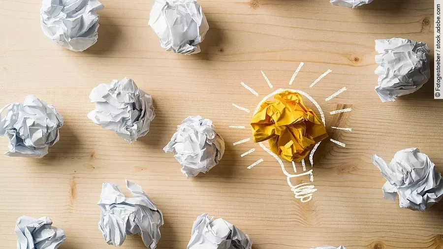 Ideen Viele zusammengeknüllte Blätter Papier. Eines davon in gelber Farbe und umrahmt wie eine leuchtende Glühbirne.