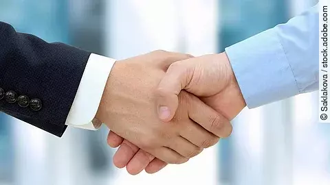 Eine Person im Anzug und eine Person im Hemd schlagen Hände ein.