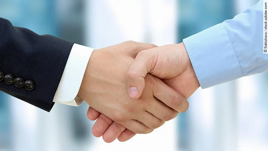 Handschlag Eine Person im Anzug und eine Person im Hemd schlagen Hände ein.
