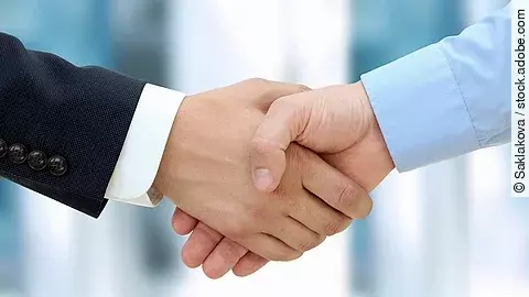 Eine Person im Anzug und eine Person im Hemd schlagen Hände ein.