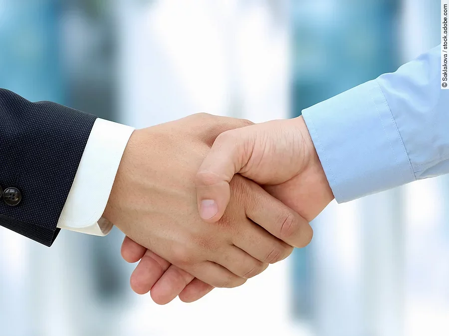 Handschlag Eine Person im Anzug und eine Person im Hemd schlagen Hände ein.
