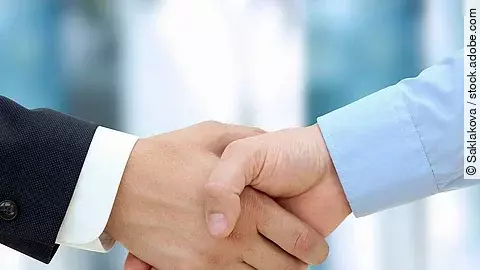 Handschlag Eine Person im Anzug und eine Person im Hemd schlagen Hände ein.