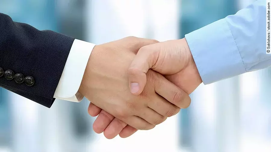 Handschlag Eine Person im Anzug und eine Person im Hemd schlagen Hände ein.