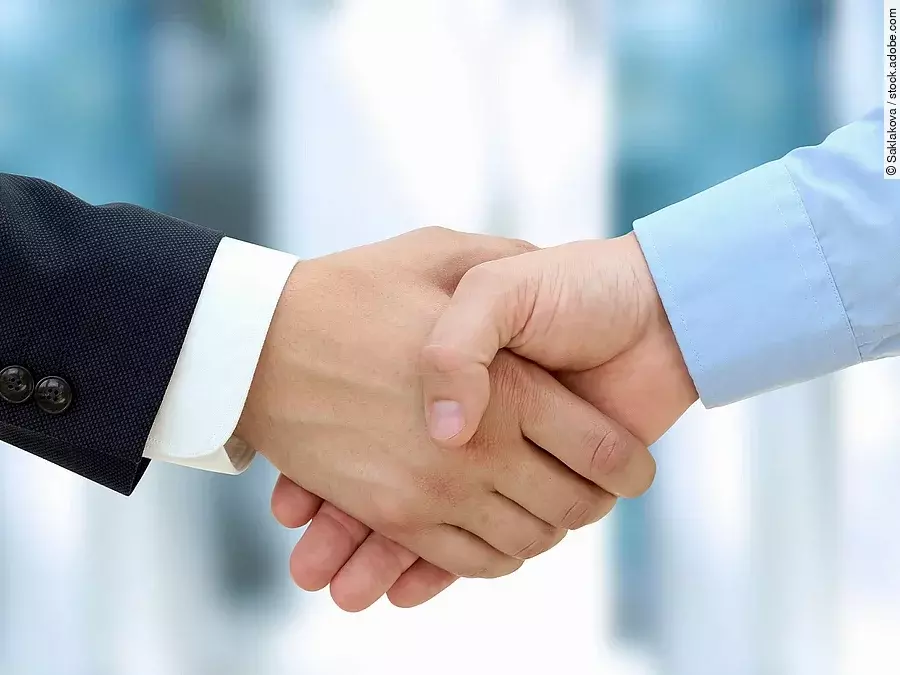 Handschlag Eine Person im Anzug und eine Person im Hemd schlagen Hände ein.