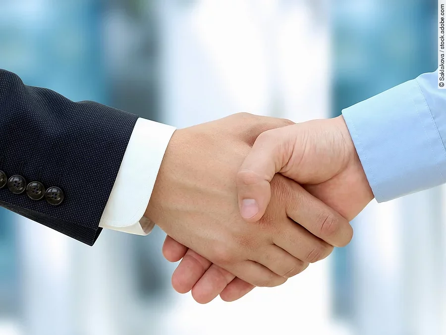 Handschlag Eine Person im Anzug und eine Person im Hemd schlagen Hände ein.