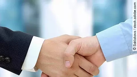 Eine Person im Anzug und eine Person im Hemd schlagen Hände ein.