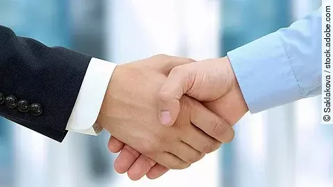 Handschlag Eine Person im Anzug und eine Person im Hemd schlagen Hände ein.