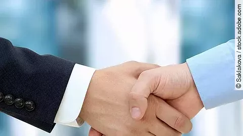 Handschlag Eine Person im Anzug und eine Person im Hemd schlagen Hände ein.