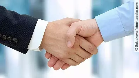 Eine Person im Anzug und eine Person im Hemd schlagen Hände ein.