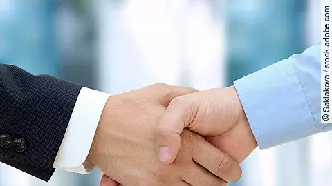 Handschlag Eine Person im Anzug und eine Person im Hemd schlagen Hände ein.