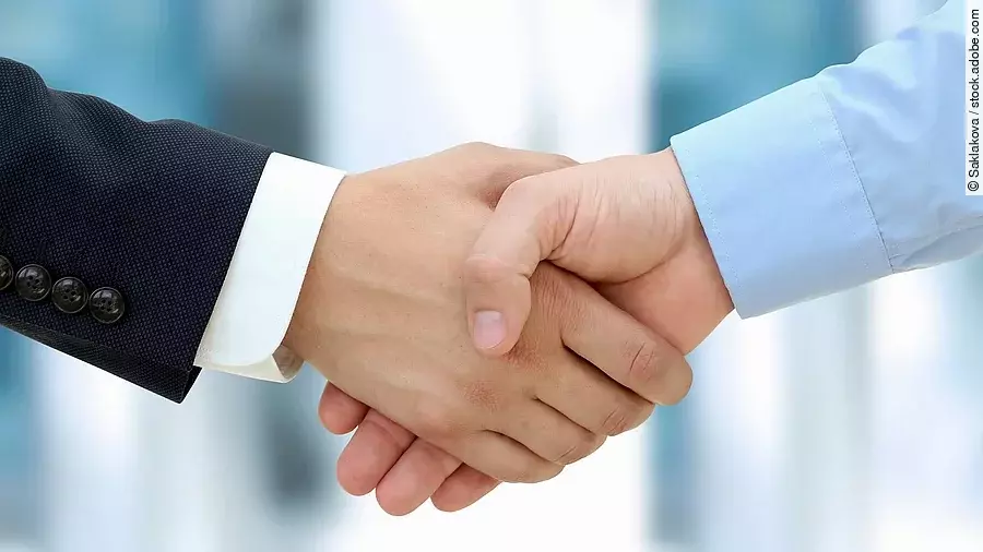 Handschlag Eine Person im Anzug und eine Person im Hemd schlagen Hände ein.