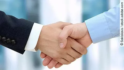 Handschlag Eine Person im Anzug und eine Person im Hemd schlagen Hände ein.