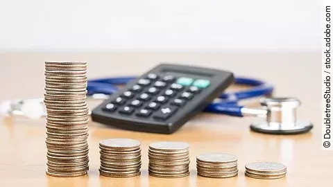 Stapel aus Münzen vor einem Taschenrechner und Stethoskop