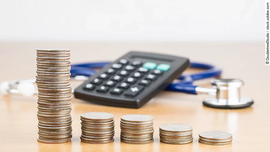 Finanzen Stapel aus Münzen vor einem Taschenrechner und Stethoskop