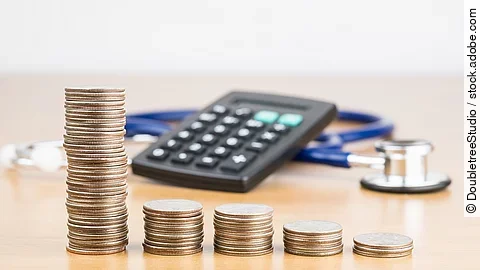 Finanzen Stapel aus Münzen vor einem Taschenrechner und Stethoskop