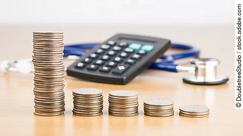 Finanzen Stapel aus Münzen vor einem Taschenrechner und Stethoskop