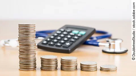 Finanzen Stapel aus Münzen vor einem Taschenrechner und Stethoskop