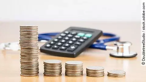 Stapel aus Münzen vor einem Taschenrechner und Stethoskop