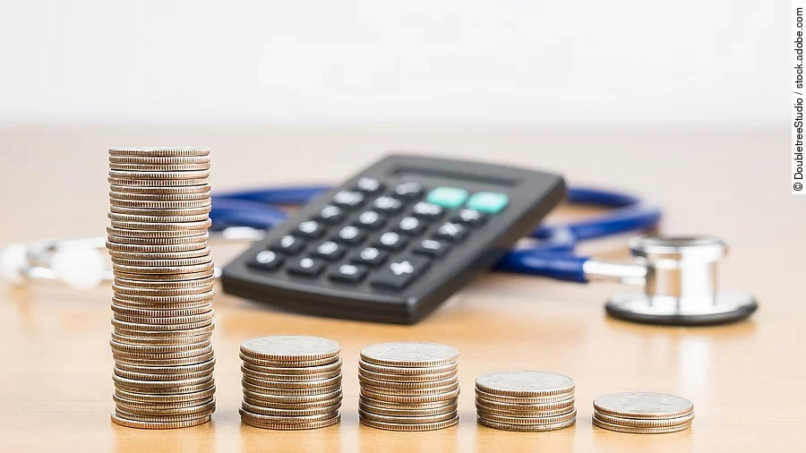 Finanzen Stapel aus Münzen vor einem Taschenrechner und Stethoskop