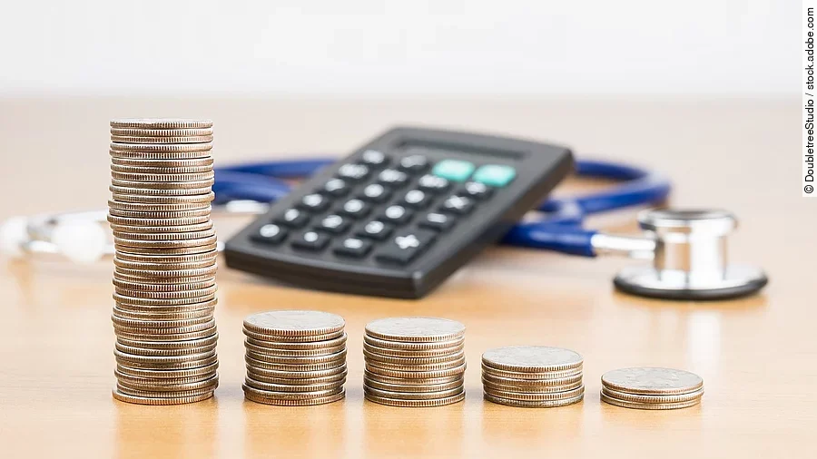Stapel aus Münzen vor einem Taschenrechner und Stethoskop