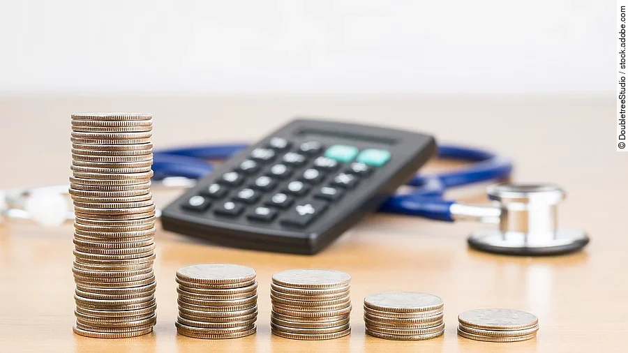 Stapel aus Münzen vor einem Taschenrechner und Stethoskop