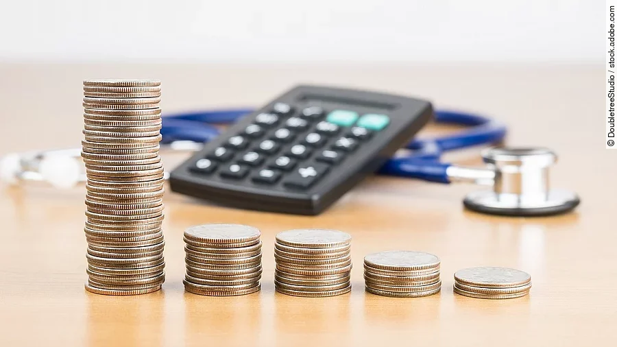 Stapel aus Münzen vor einem Taschenrechner und Stethoskop