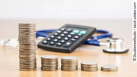 Finanzen Stapel aus Münzen vor einem Taschenrechner und Stethoskop