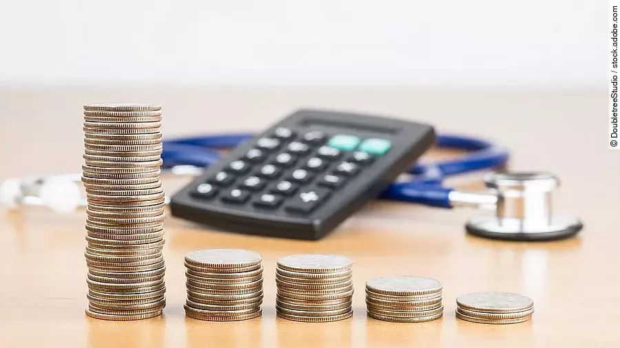 Finanzen Stapel aus Münzen vor einem Taschenrechner und Stethoskop