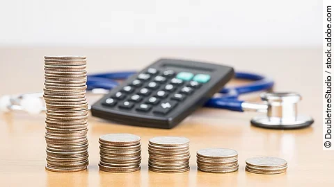 Finanzen Stapel aus Münzen vor einem Taschenrechner und Stethoskop